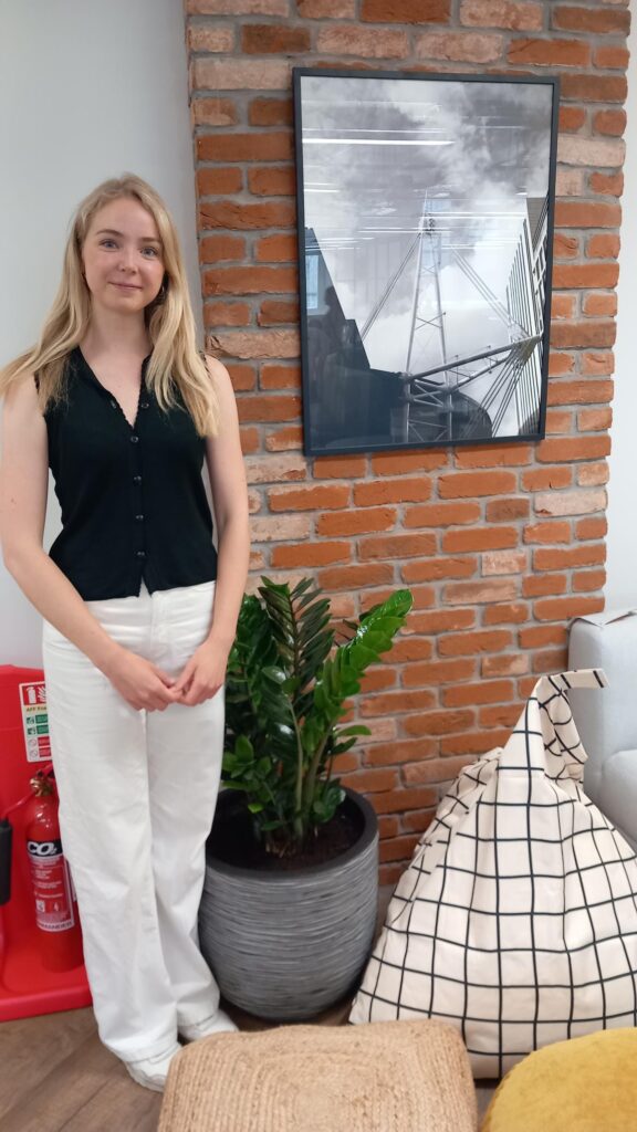 Caroline, étudiante en design chez Paramount, se tient fièrement devant sa photographie présentée sur le mur du client Menzies dans l'aménagement final du bureau