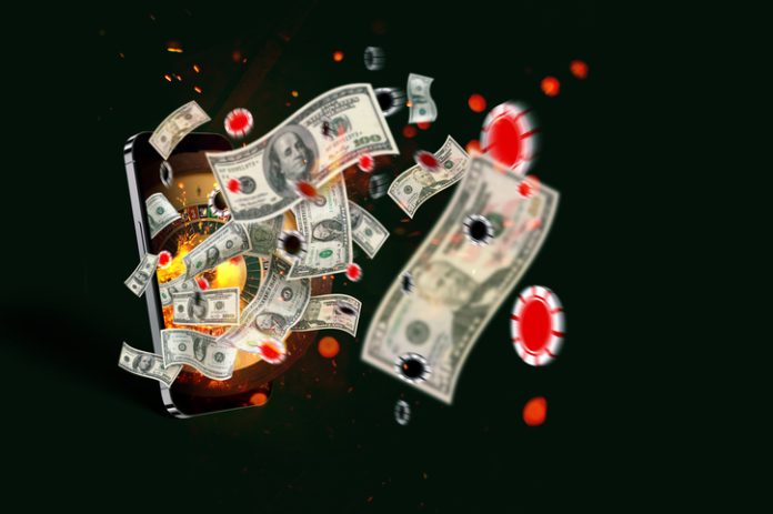 Casino en ligne, concept. Smartphone avec roulette, dollars volants et jetons avec étincelles sur fond vert foncé. Journée créative gagnante. Application de paris et de jeu Application de paris et de jeu pour la stratégie gagnante