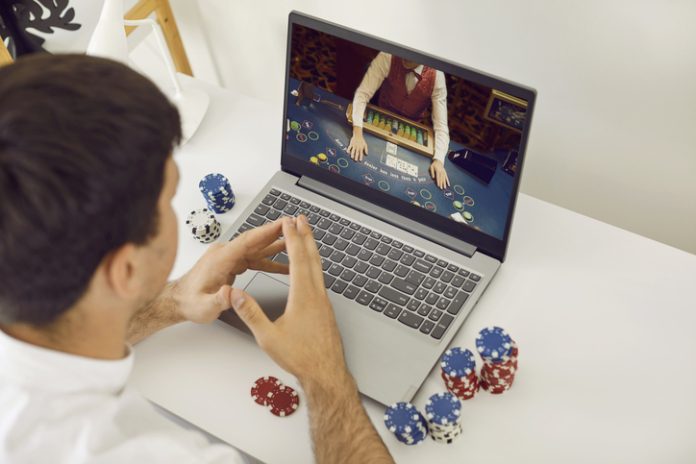 Jeune joueuse de poker en ligne smart masculin relaxante sur son ordinateur portable à la maison. Tendance du casino en ligne