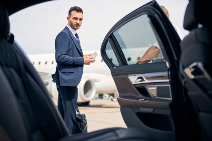 Homme d'affaires prospère debout près de la voiture et ayant l'air déterminé Service de prise en charge à l'aéroport de Logan